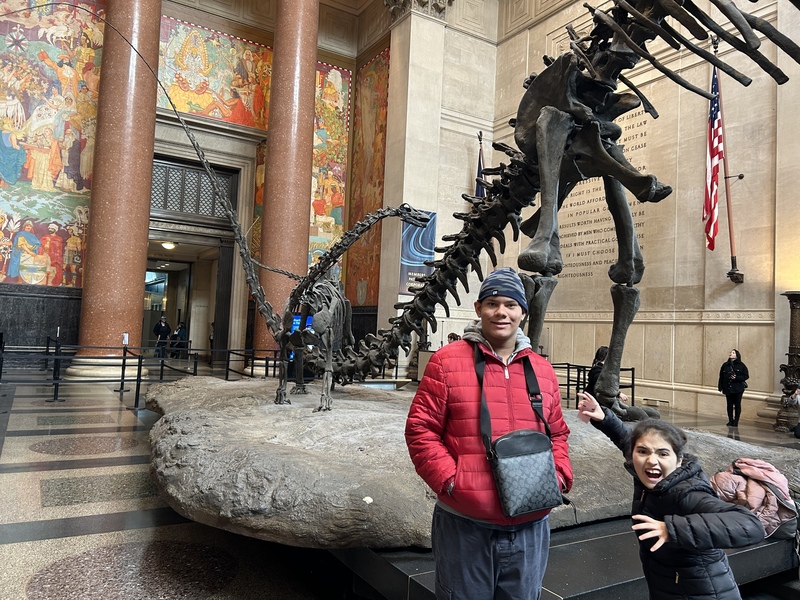 Two students pose in front of a dinosaur skeleton