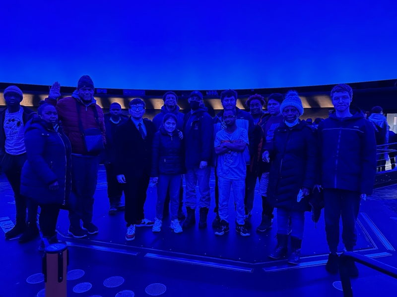 Everyone in the trip poses together under blue lighting in the museum