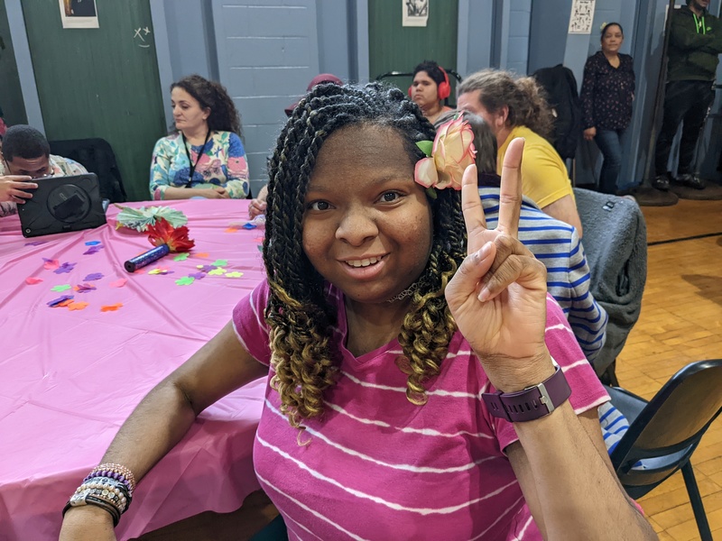 a student sitting at a table poses for a selfie and gives the peace sign